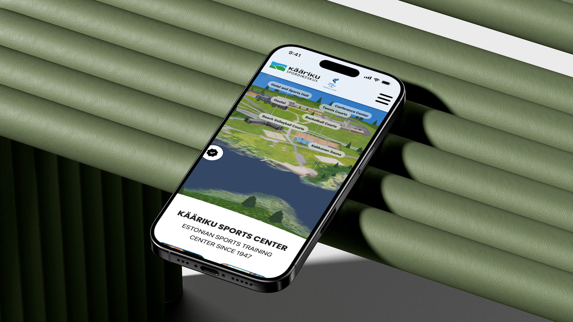 A smartphone rests on a green surface, showcasing an iphone with Kaariku Sports Center website open.